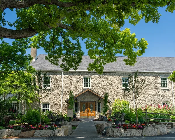 Exterior view of the Gideon Owen Wine Company stone building with a landscaped entrance and large tree.