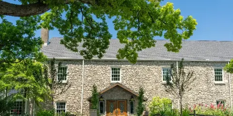 Exterior view of the Gideon Owen Wine Company stone building with a landscaped entrance and large tree.