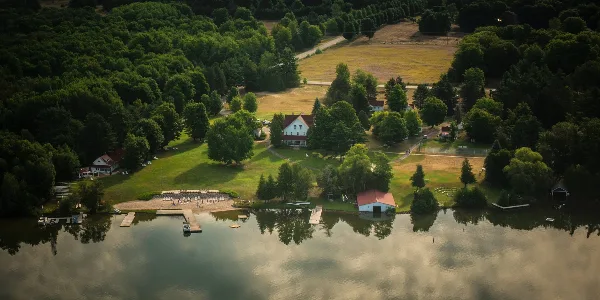 Aerial view of a historic waterfront resort featuring a large white hotel, multiple cottages, and a sandy beach on a lake surrounded by dense forest.