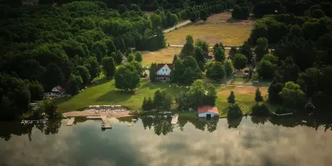 Aerial view of a historic waterfront resort featuring a large white hotel, multiple cottages, and a sandy beach on a lake surrounded by dense forest.