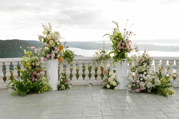 Large floral arrangement with white columns and mixed flowers on a terrace overlooking a body of water.