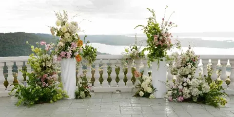 Large floral arrangement with white columns and mixed flowers on a terrace overlooking a body of water.
