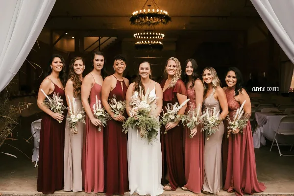 A bride and bridesmaids posing inside a rustic barn wedding venue with chandeliers and white drapery.