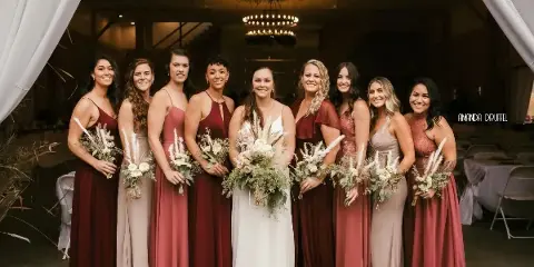 A bride and bridesmaids posing inside a rustic barn wedding venue with chandeliers and white drapery.