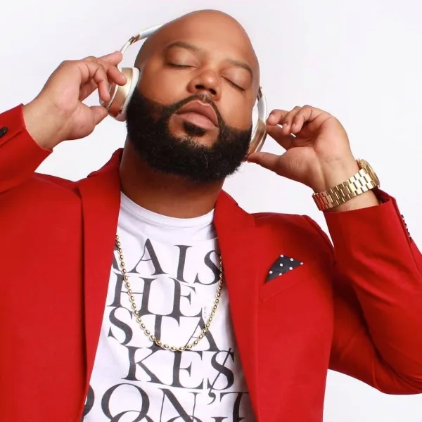 Portrait of a bearded man in a red blazer wearing gold headphones and a gold chain.