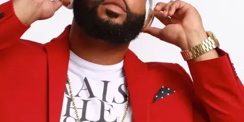 Portrait of a bearded man in a red blazer wearing gold headphones and a gold chain.