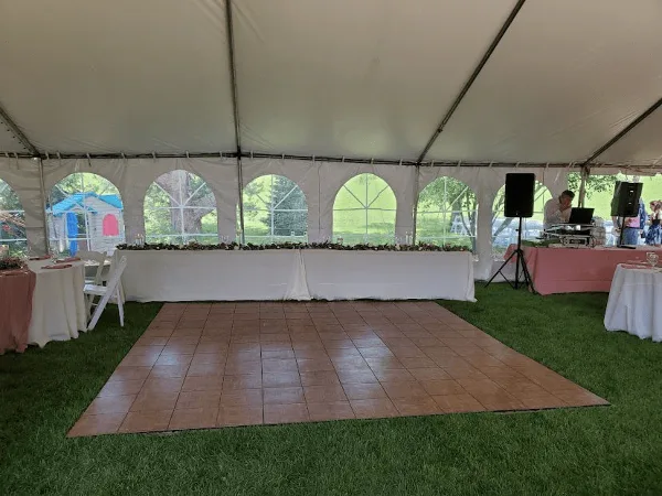 Interior view of a white event tent set up on a lawn with a dance floor, tables, and chairs.