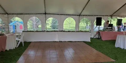 Interior view of a white event tent set up on a lawn with a dance floor, tables, and chairs.