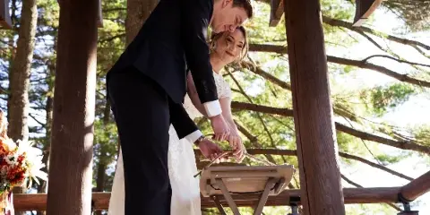 A bride and groom performing a unity candle ceremony at an outdoor wooden pavilion.