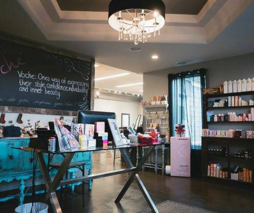 Interior view of Salon Voche showing a retail display table, product shelves, and a chalkboard sign.