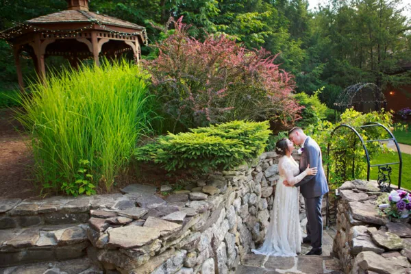 A bride and groom sharing a kiss on a stone staircase in a garden setting with a gazebo in the background.