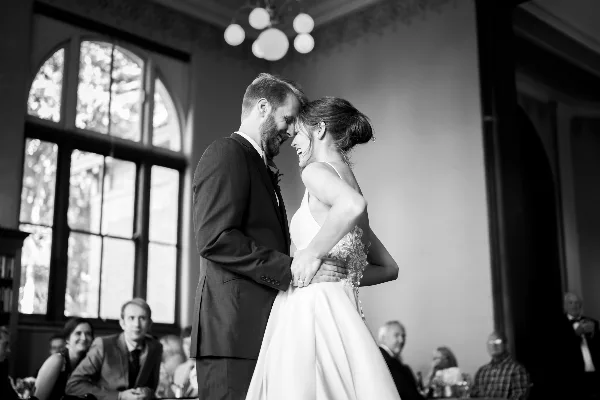 Black-and-white photo of a bride and groom smiling and touching foreheads during a wedding reception.