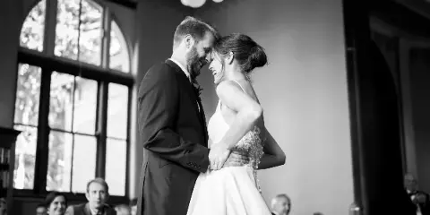 Black-and-white photo of a bride and groom smiling and touching foreheads during a wedding reception.