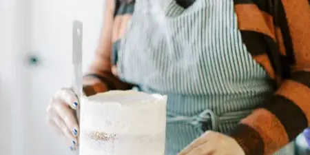 A baker wearing a striped apron is frosting a cake on a turntable.