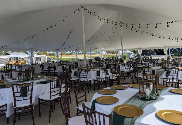Interior of a white wedding tent with set tables, chairs, and string lights.