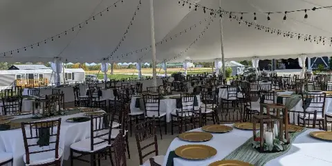 Interior of a white wedding tent with set tables, chairs, and string lights.