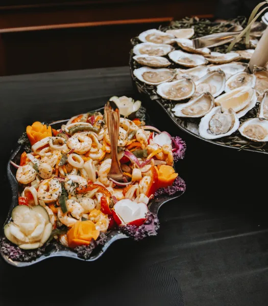 A catering table featuring a platter of shrimp cocktail and a tray of fresh oysters on the half shell.