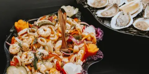 A catering table featuring a platter of shrimp cocktail and a tray of fresh oysters on the half shell.