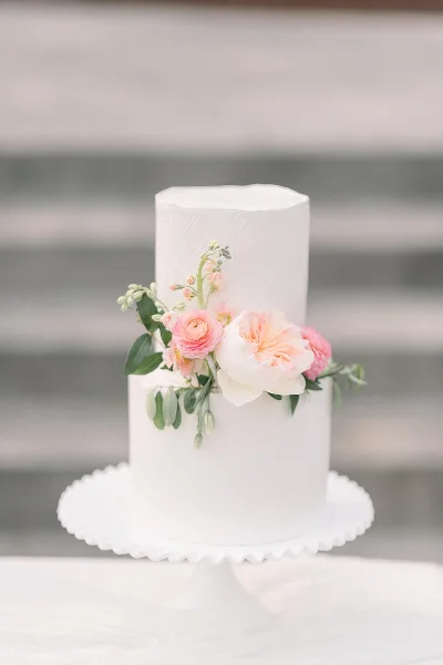 A two-tier white wedding cake decorated with pink and white flowers on a white cake stand.