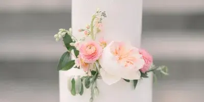 A two-tier white wedding cake decorated with pink and white flowers on a white cake stand.