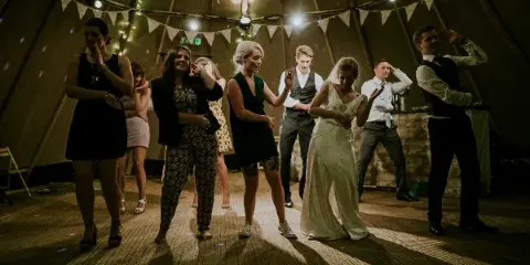 Guests dancing at a wedding reception in a tented venue.