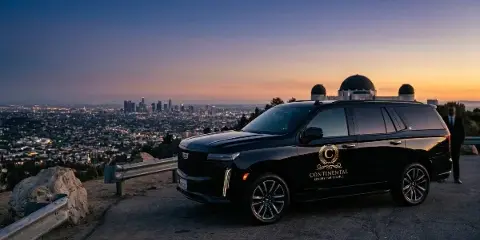 Black Cadillac Escalade ESV with Continental Luxury Car Service logo parked at a Los Angeles overlook with a chauffeur standing nearby