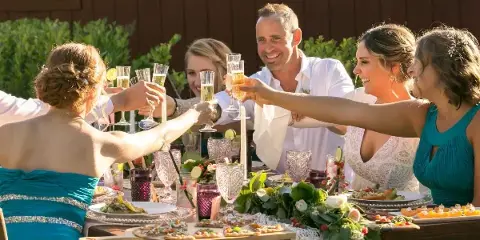 A bride and groom toast with their wedding party at a catered reception table.
