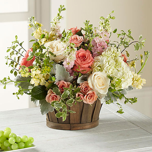 A mixed bouquet of pink and white roses, hydrangeas, and greenery in a wooden basket.
