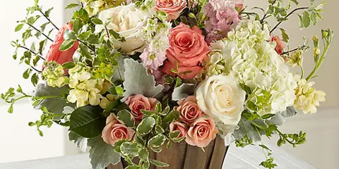 A mixed bouquet of pink and white roses, hydrangeas, and greenery in a wooden basket.