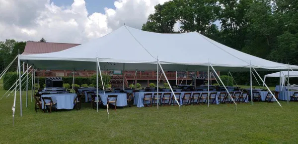 Large white event tent set up on a grassy lawn with rows of tables and chairs arranged underneath.