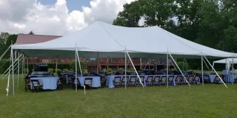 Large white event tent set up on a grassy lawn with rows of tables and chairs arranged underneath.
