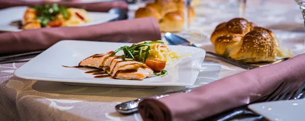 A plated meal featuring sliced chicken, salad, and bread rolls on a set dining table.