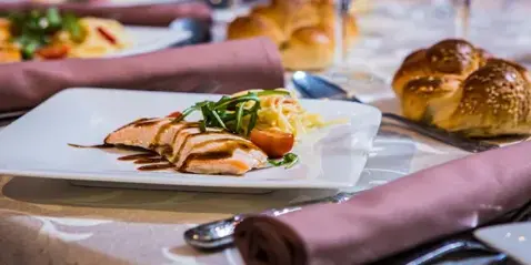 A plated meal featuring sliced chicken, salad, and bread rolls on a set dining table.