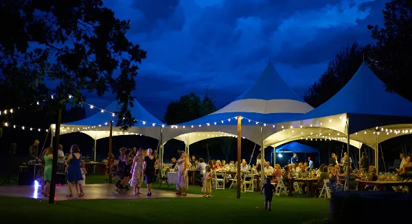 A large white event tent illuminated at night with tables and chairs set up for a gathering.