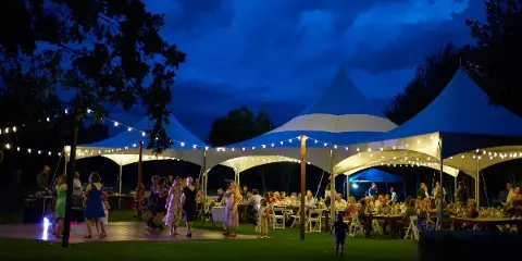 A large white event tent illuminated at night with tables and chairs set up for a gathering.