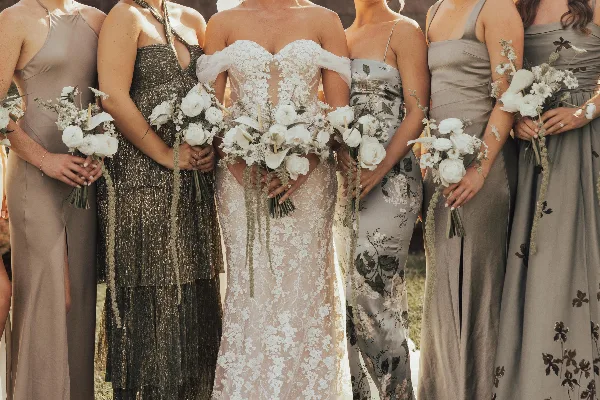 A bride and bridesmaids holding white floral bouquets featuring orchids, roses, and ranunculus.