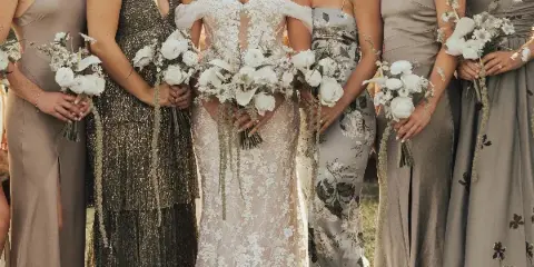 A bride and bridesmaids holding white floral bouquets featuring orchids, roses, and ranunculus.