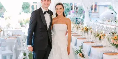 A bride and groom standing together at a wedding reception with the bride wearing a white floral gown and styled hair.