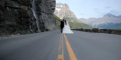 A bride and groom kissing on a paved road with a waterfall and mountains in the background.