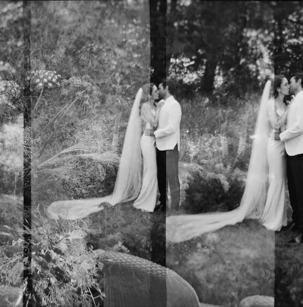 Black and white photograph of a bride and groom kissing in a garden setting.