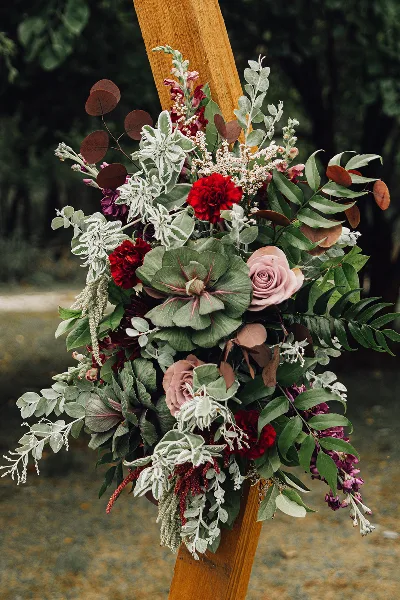 A detailed floral arrangement with red and pink roses, green foliage, and white filler flowers attached to a wooden beam.