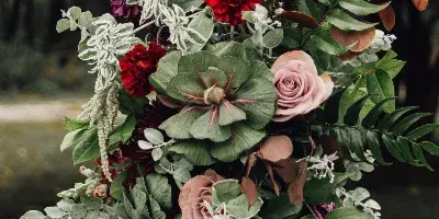 A detailed floral arrangement with red and pink roses, green foliage, and white filler flowers attached to a wooden beam.