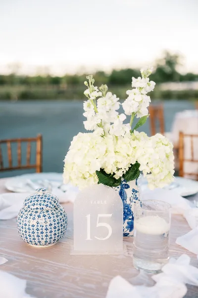 Outdoor wedding table setting with white floral centerpiece and table number 15, overlooking a lake.
