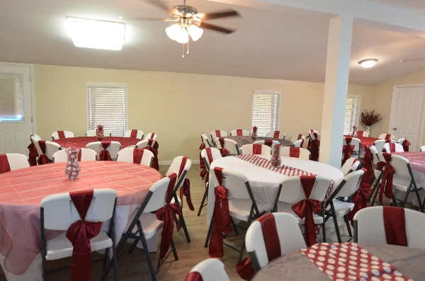 Interior view of an event venue with round tables set with red and white tablecloths and chairs decorated with red sashes.
