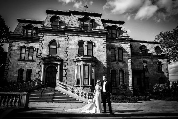 A black and white photograph of a bride and groom standing on the steps of a large stone building.