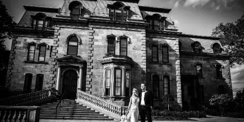 A black and white photograph of a bride and groom standing on the steps of a large stone building.