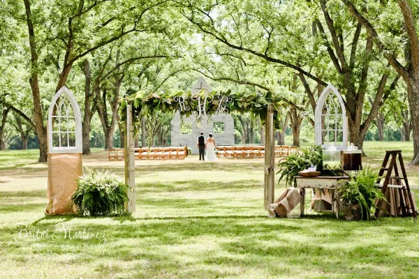 A wedding ceremony setup at an outdoor farm venue with a decorated arch, seating, and a couple.