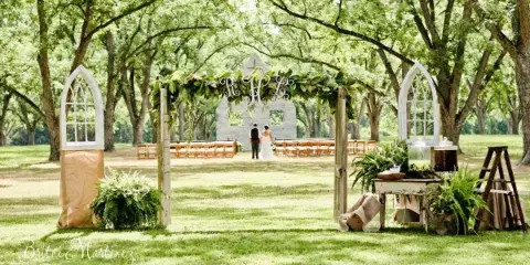 A wedding ceremony setup at an outdoor farm venue with a decorated arch, seating, and a couple.