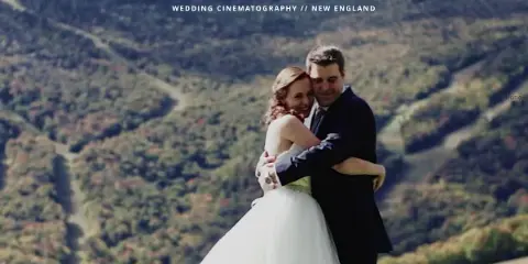 A bride and groom embracing in a wedding dress and suit against a backdrop of rolling green hills.