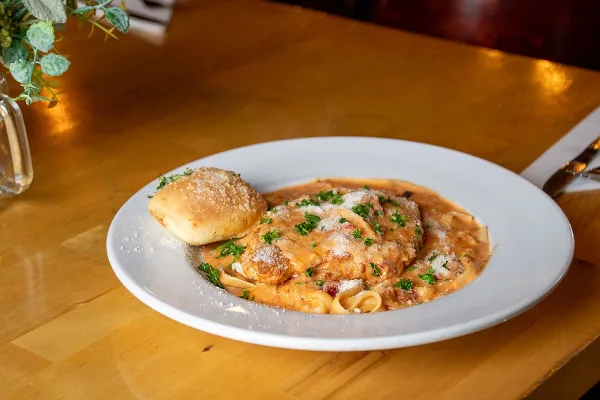 Plated chicken parmesan over fettuccine with garlic bread on a wooden table